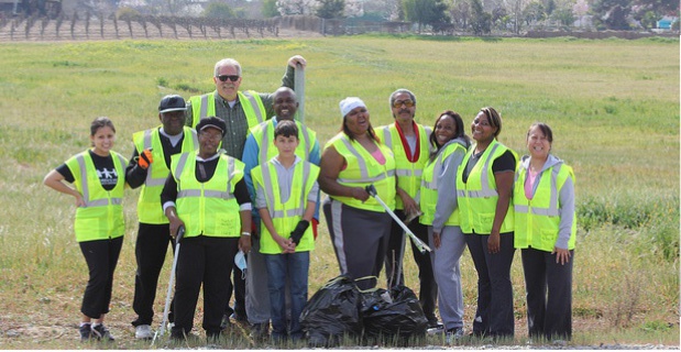 Photo of a group of volunteers  with trash picking devices and trash bags cleaning up a field